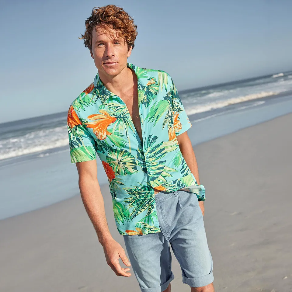 En man b&auml;r en f&auml;rgglad hawaiiskjorta och ljusa shorts p&aring; stranden.

