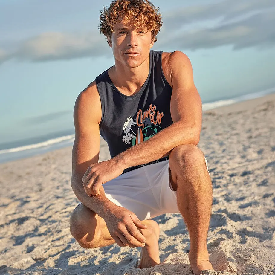 Man b&auml;r ett bl&aring;tt linne med motiv och vita shorts p&aring; stranden.

