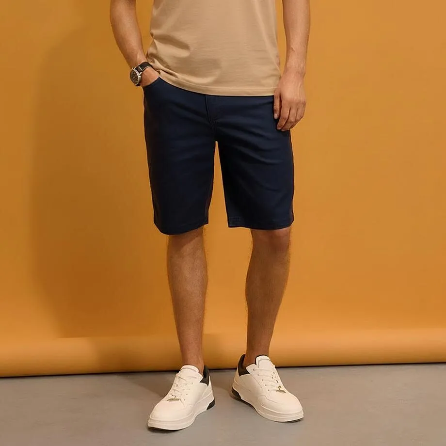 Beige T-shirt, m&ouml;rkbl&aring; shorts och vita sneakers.