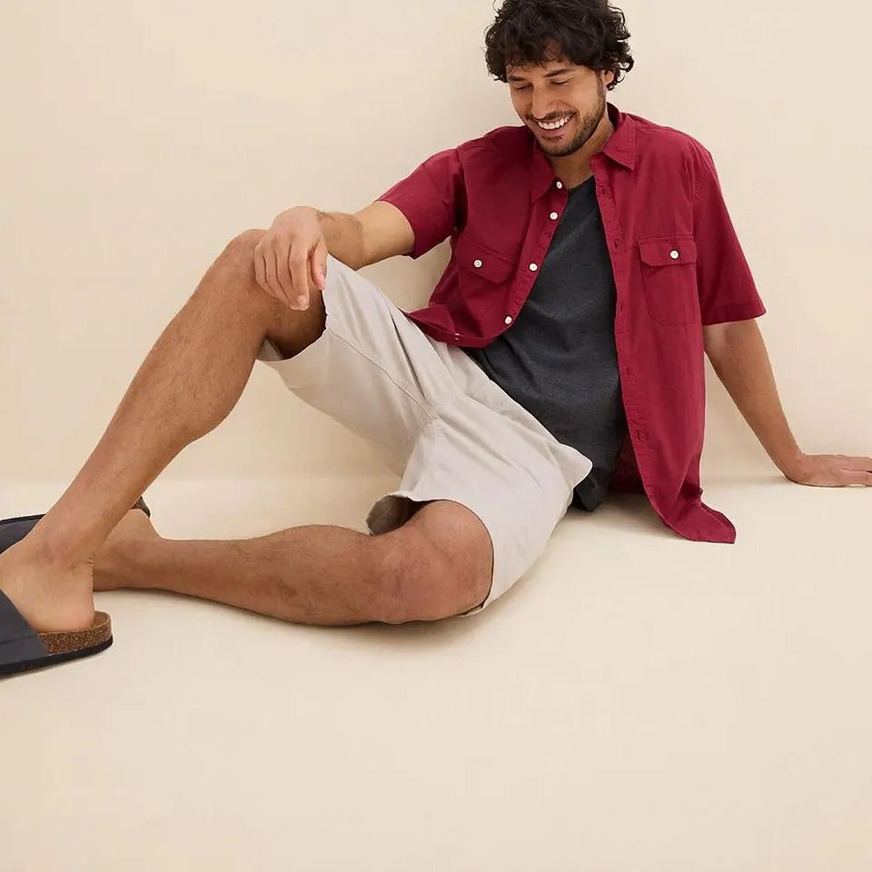 R&ouml;d kort&auml;rmad skjorta &ouml;ver en m&ouml;rk tr&ouml;ja, tillsammans med ljusa shorts och bekv&auml;ma sandaler.