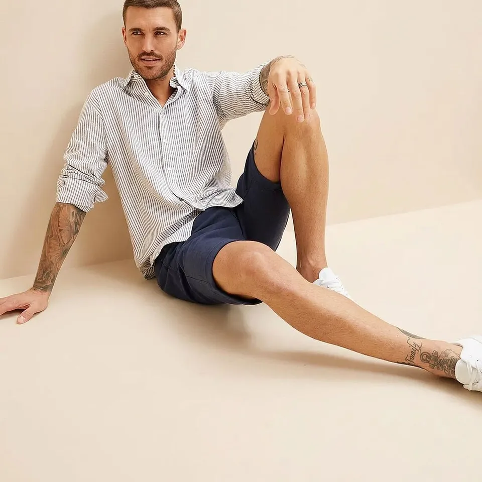 Han b&auml;r en randig skjorta, m&ouml;rkbl&aring; shorts och vita sneakers.

