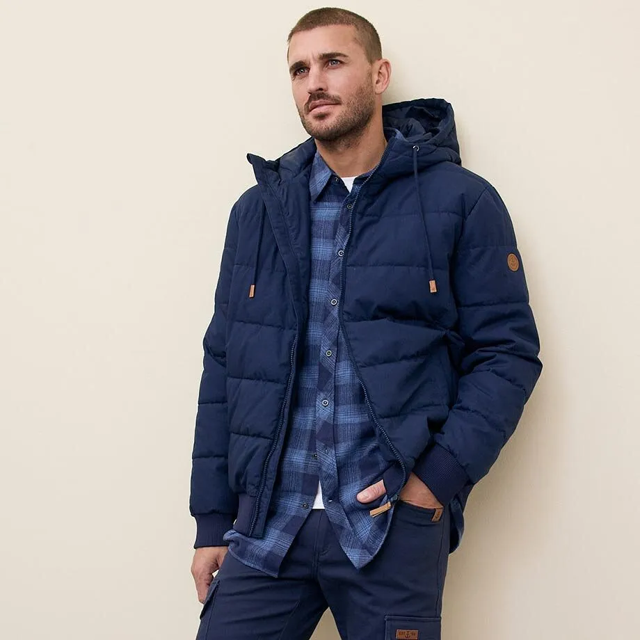 M&ouml;rkbl&aring; vinterjacka med huva &ouml;ver en rutig skjorta.

