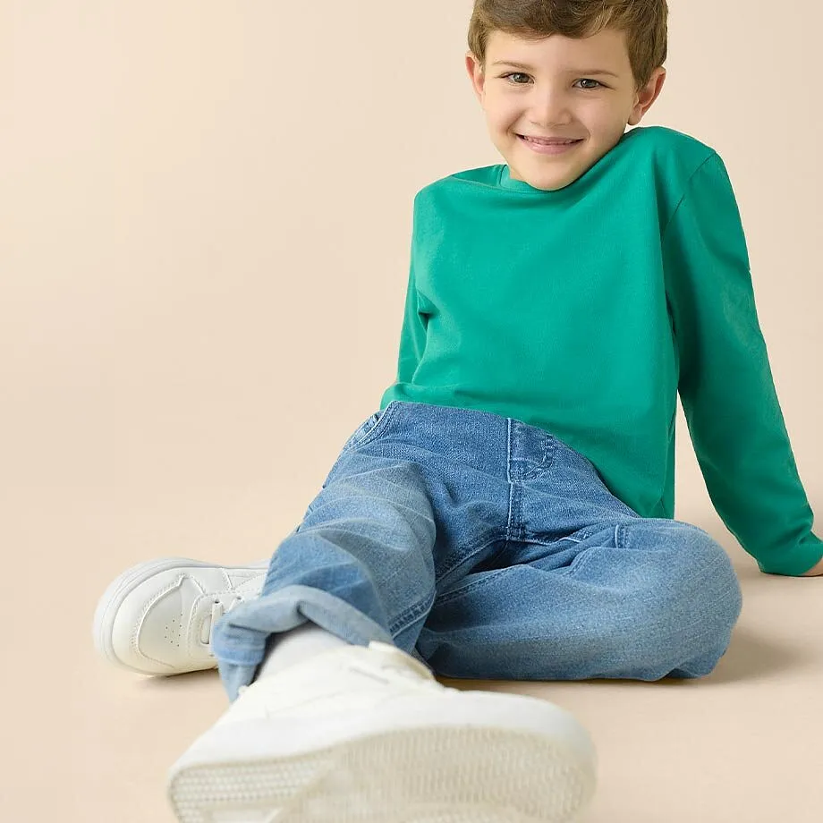 Gr&ouml;n l&aring;ng&auml;rmad tr&ouml;ja, bl&aring; jeans och vita sneakers &ndash; en bekv&auml;m outfit f&ouml;r barn.