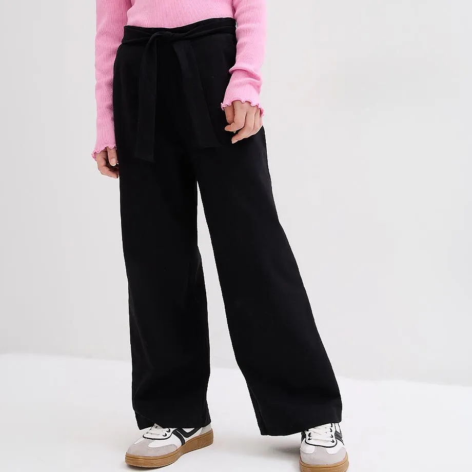 Rosa topp, svarta vida byxor med knytband och sportiga sneakers.