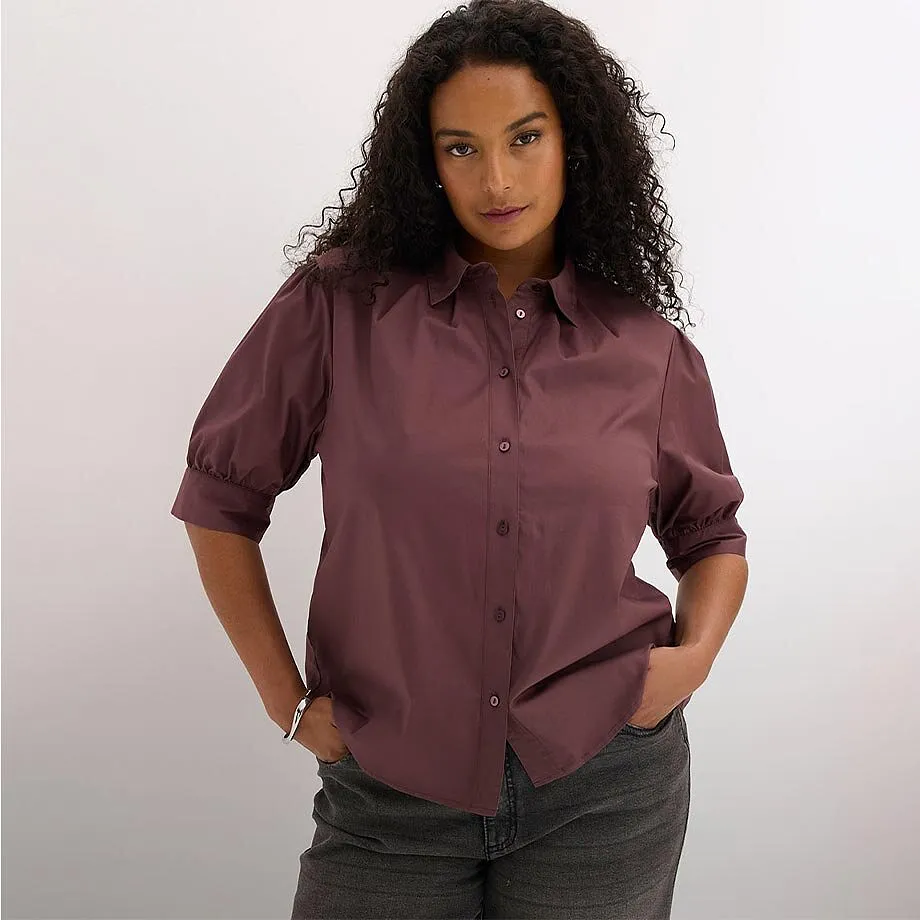 Bordeauxr&ouml;d blus med eleganta puff&auml;rmar och krage, tillsammans med m&ouml;rka jeans.