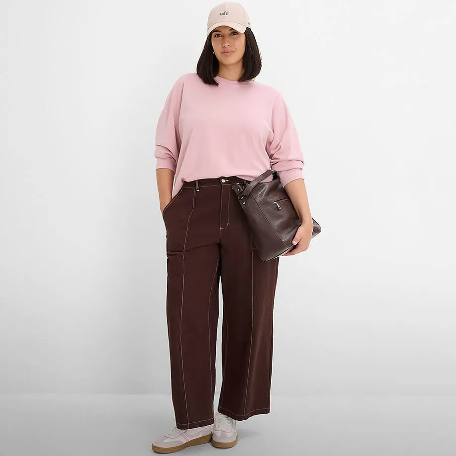 Rosa sweatshirt, brun, vid byxa med dekorativa s&ouml;mmar, beige keps och m&ouml;rk v&auml;ska.