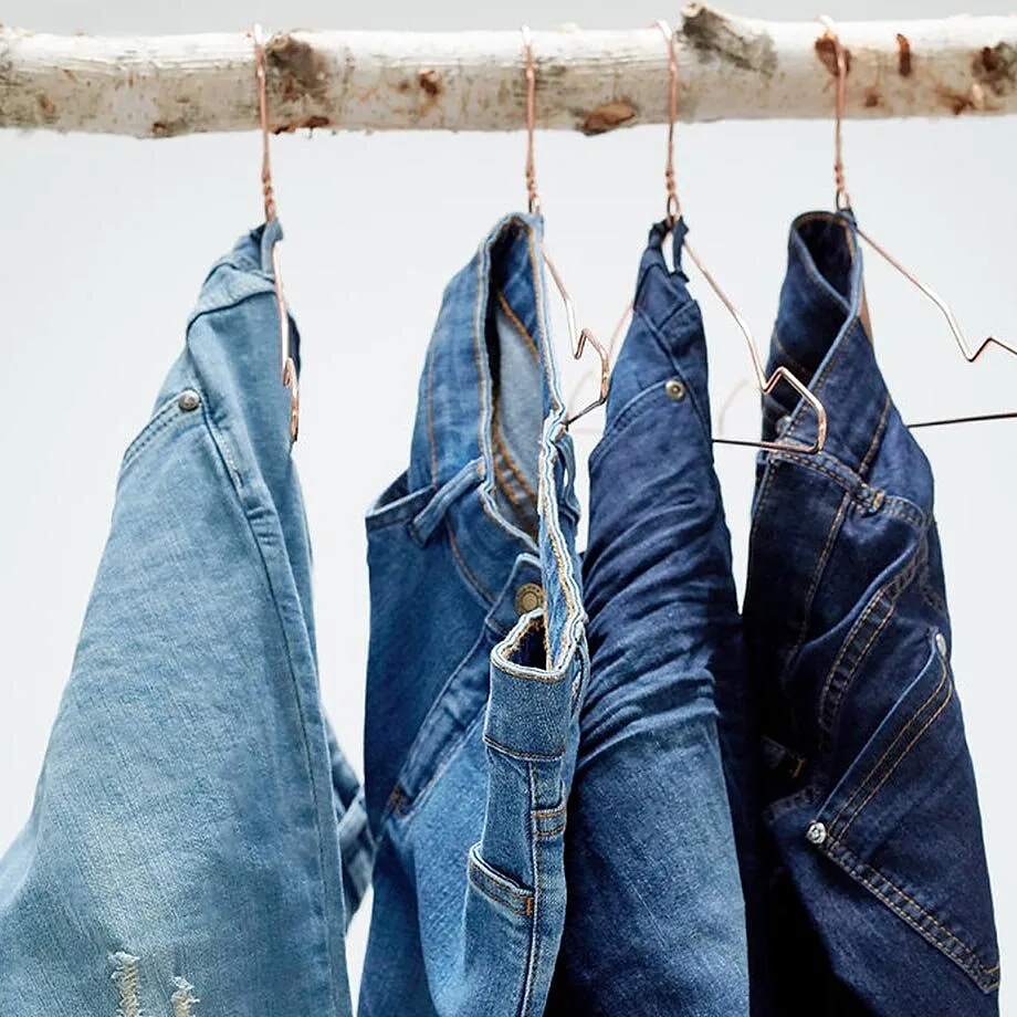 En rad bl&aring;a jeans med olika tv&auml;ttningar h&auml;nger stabilt p&aring; galgar.