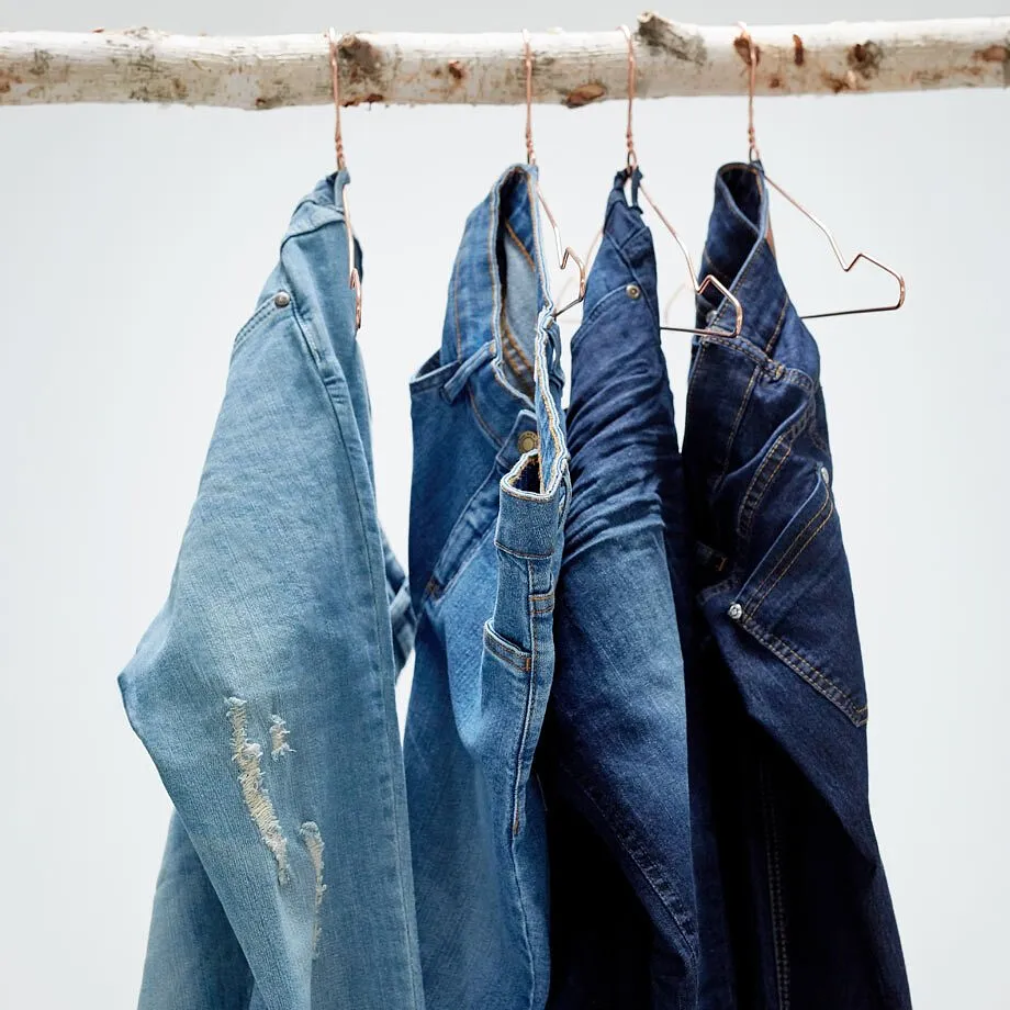 Jeans i olika bl&aring; nyanser h&auml;nger p&aring; galgar p&aring; en tr&auml;gren.