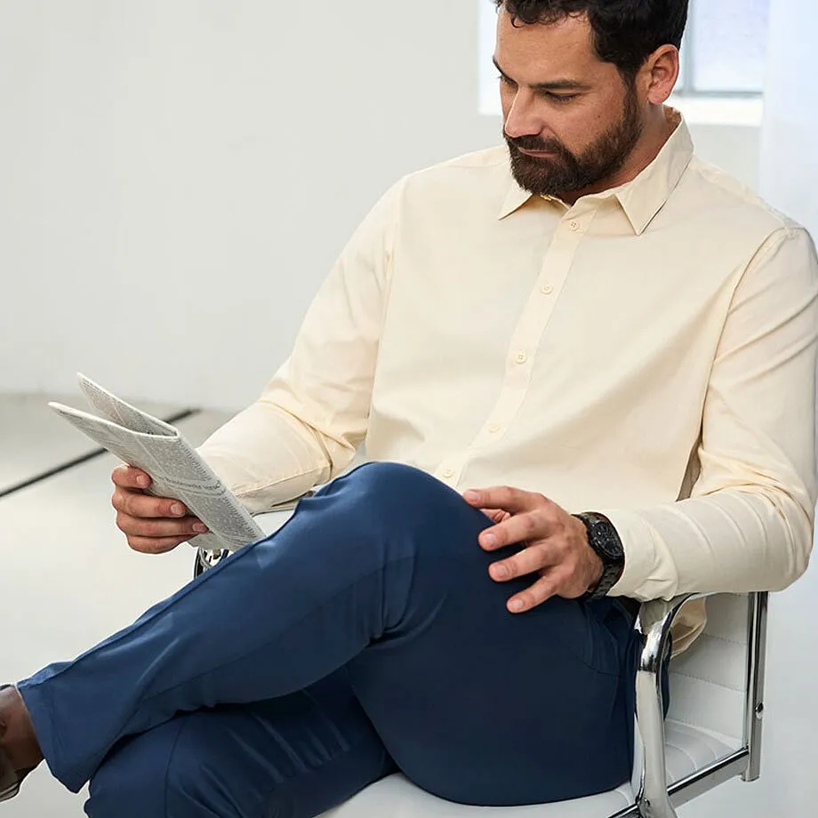 Mannen har p&aring; sig en beige skjorta, m&ouml;rkbl&aring; byxor och ett svart armbandsur.
