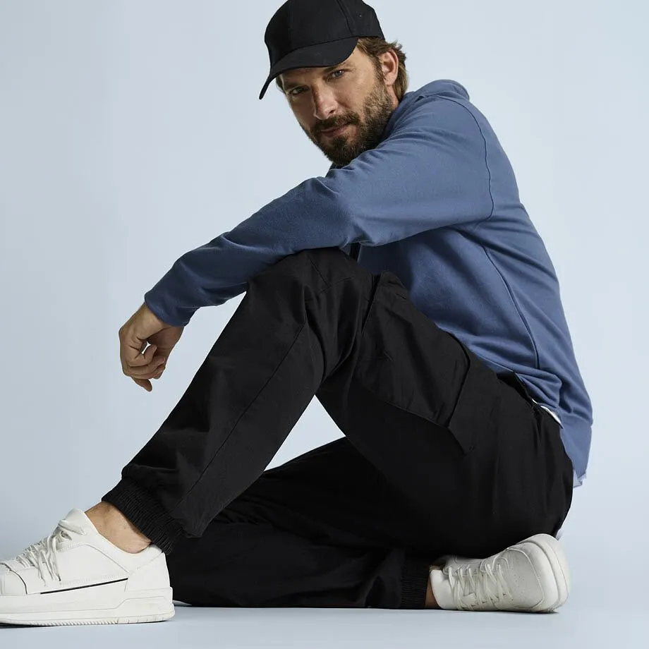 Ledig look: svart keps, bl&aring; huvtr&ouml;ja, bekv&auml;ma svarta cargobyxor och vita sneakers. 