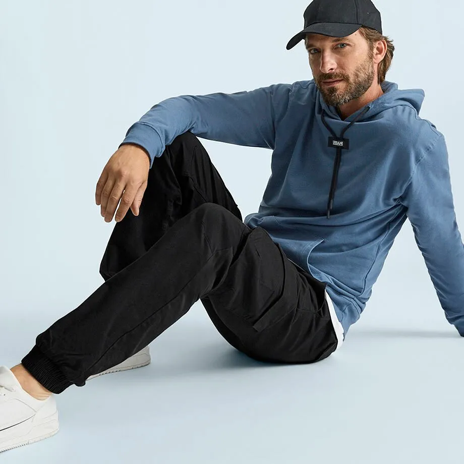 Mannen har p&aring; sig en bl&aring; huvtr&ouml;ja, svarta cargobyxor, vita sneakers och keps.