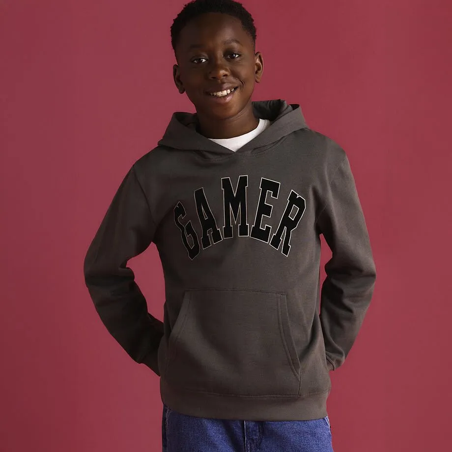 Gr&aring; och svart huvtr&ouml;ja med "Gamer"-tryck och ett par bl&aring; jeans.