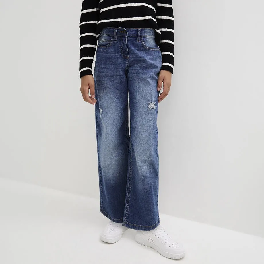Barnet har p&aring; sig en randig, l&aring;ng&auml;rmad T-shirt, bl&aring;, utsv&auml;ngda jeans och vita sneakers.