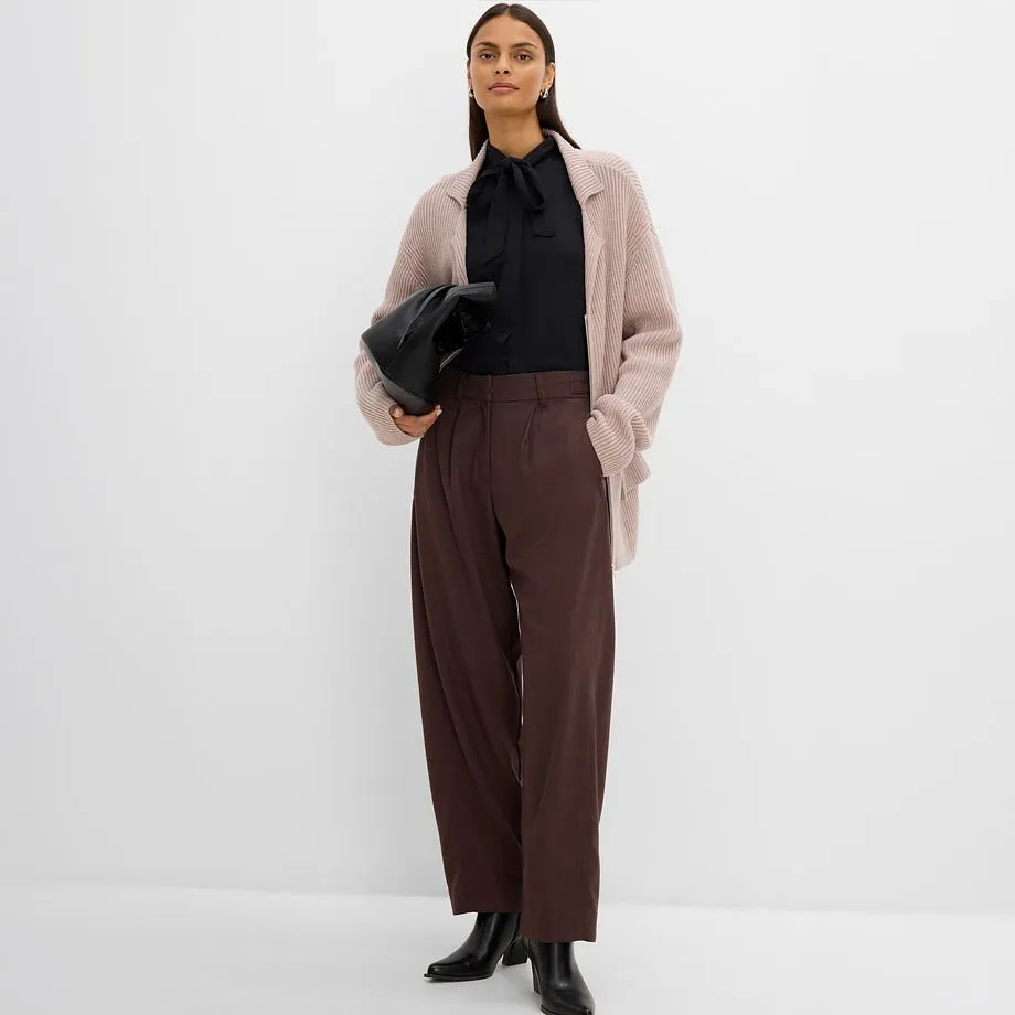 Hon har p&aring; sig en svart blus, beige cardigan, bruna byxor och svarta st&ouml;vletter.
