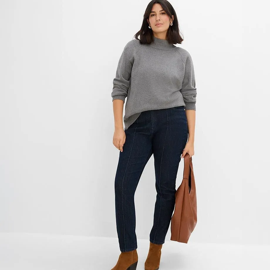 Gr&aring; tr&ouml;ja med st&aring;krage, m&ouml;rka jeans med s&ouml;mmar, bruna st&ouml;vletter och v&auml;ska.