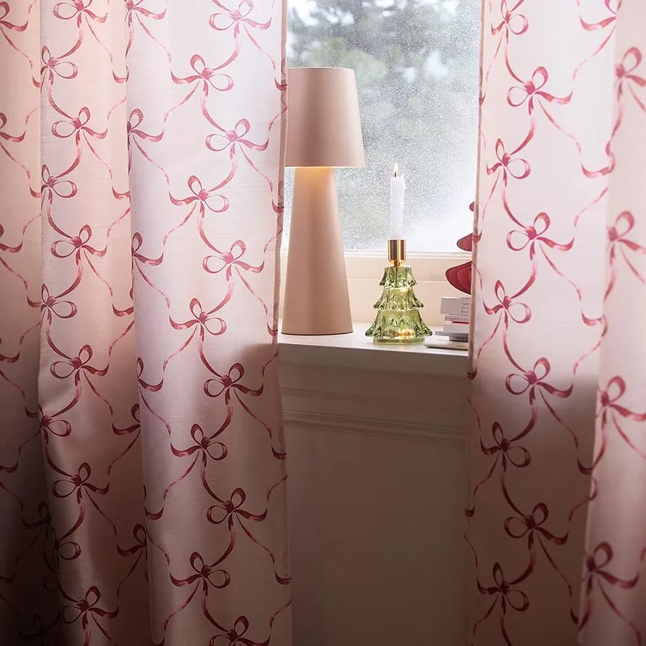 Rosa gardiner med rosettm&ouml;nster pryder f&ouml;nstret tillsammans med lampa och ljus.