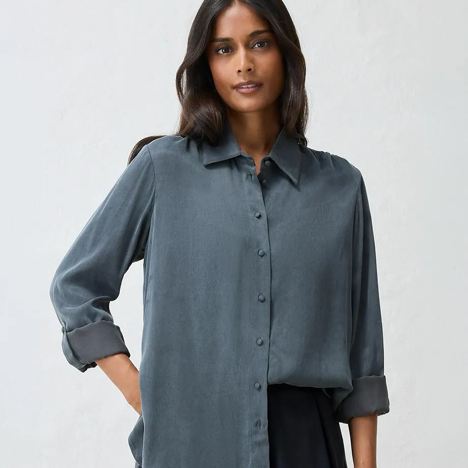 Kvinnan har p&aring; sig en elegant, m&ouml;rkgr&aring; blus och en stilren, svart kjol.