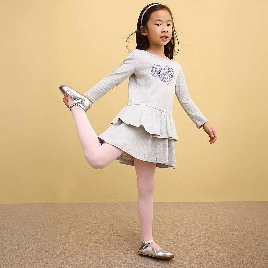 En flicka har p&aring; sig en gr&aring; kl&auml;nning med volanger och rosa leggings.