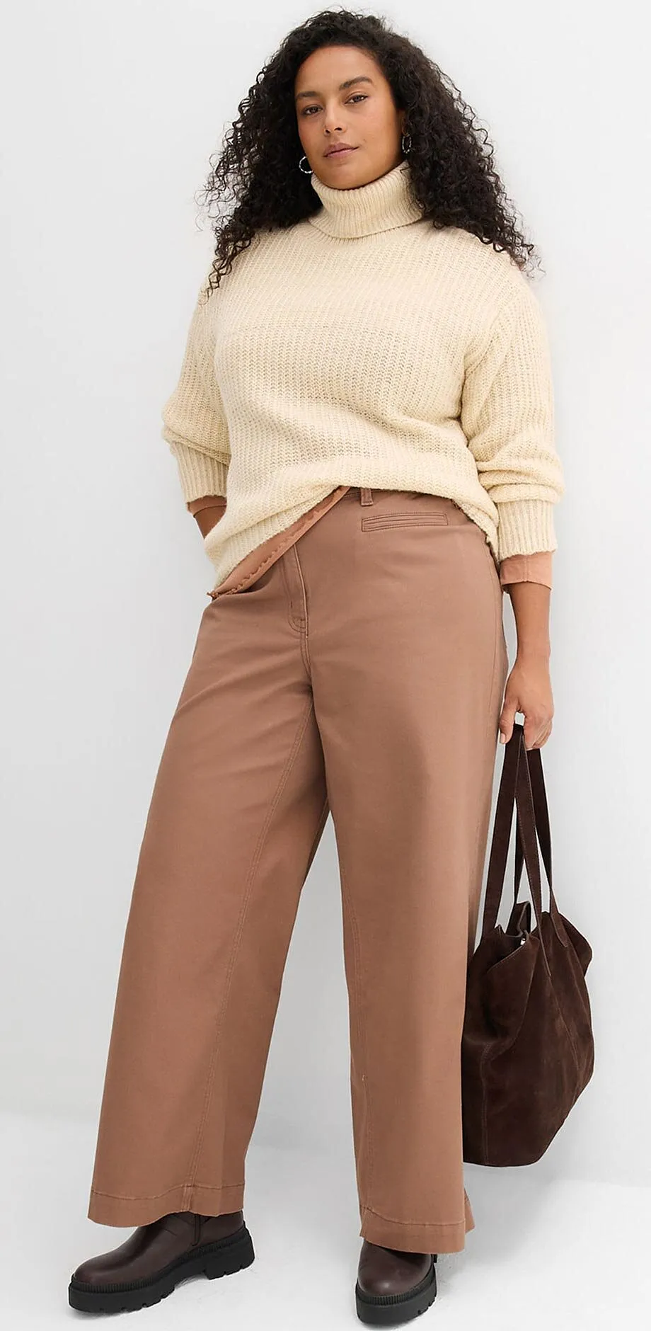 Stickad tr&ouml;ja i creme och d&auml;rtill ett par bruna byxor.

